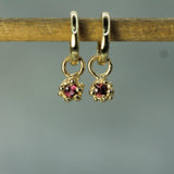 Gold earrings with rubies on a wooden stick against a gray background