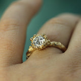 A close-up of a hand wearing a gold ring with a 1ct round lab-grown diamond in a textured halo setting.