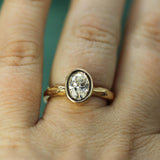 A close-up of a gold ring with an oval lab-grown diamond worn on a finger.