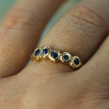 A close-up of a gold ring with five round-cut blue gemstones worn on a finger.