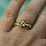 A close-up of a hand wearing a yellow gold ring with a brilliant-cut lab-grown diamond in a bezel setting.