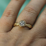 A close-up of a hand wearing a yellow gold ring with a brilliant-cut lab-grown diamond in a bezel setting.