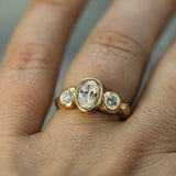 A yellow gold three-stone ring with a central oval lab-grown diamond and two smaller lab-grown diamonds on either side, shown worn on a finger.