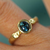 A close-up of an 18k yellow gold ring with a faceted dark blue oval sapphire, worn on a finger.