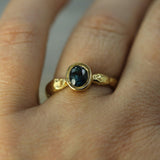 An 18k yellow gold ring with an oval dark blue sapphire, worn on a person's finger.