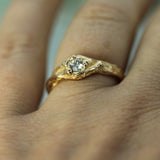A close-up of a hand wearing a gold ring with a textured organic-shaped band and a lab-grown diamond.