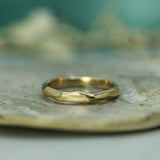 A gold ring with a textured, organic shape resting on a light-colored stone surface with a soft teal background.