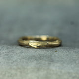 A textured, organic-shaped gold ring resting on a neutral gray surface.
