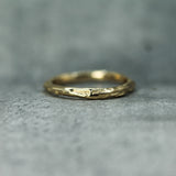 A textured gold ring with an organic, ocean-like surface detail, resting on a gray stone surface.