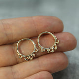 Gold hoop earrings held between fingers against a blurred background