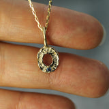 Gold necklace with a circular pendant held between fingers against a neutral background