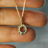 Gold necklace with a circular pendant held between fingers.