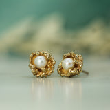 Gold earrings with pearl centers on a blurred background