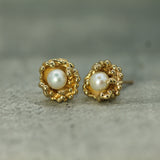 Gold earrings with pearl centers on a textured surface
