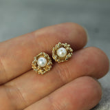 Gold earrings with pearls held between fingers against a blurred background
