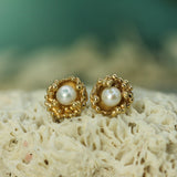 Gold earrings with pearls on a textured surface