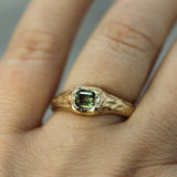 14k yellow gold signet ring with a green sapphire on a finger against a neutral background