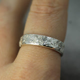 Silver ring with a textured band worn on a finger against a neutral background