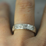 Silver ring with a textured band on a finger against a neutral background