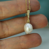 Gold necklace with a pearl pendant held between fingers against a blurred background