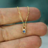 Gold necklace with a blue sapphire pendant held between fingers against a blurred background