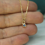 Gold necklace with a blue sapphire pendant held between fingers