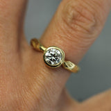 Gold ring with a diamond on a finger against a neutral background