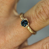 Gold ring with a blue sapphire on a finger against a neutral background