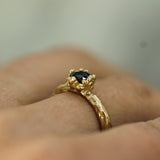 Gold ring with a blue sapphire on a finger against a neutral background