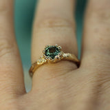 Gold ring with a green sapphire on a finger against a blurred background
