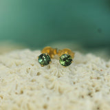 Gold earrings with teal sapphires on a textured surface with a blurred green background