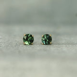 Pair of teal sapphire stud earrings on a neutral background