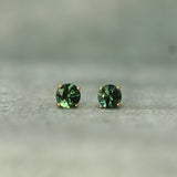 Pair of teal sapphire stud earrings on a neutral background