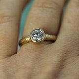 14k Yellow gold ring with a diamond on a person's finger against a light blue background