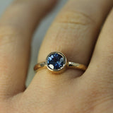 Gold ring with a blue sapphire on a finger against a neutral background