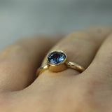 Gold ring with a blue sapphire on a finger against a blurred background