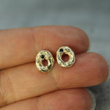 Gold earrings with dark blue sapphires held between fingers against a neutral background