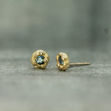 Gold stud earrings with a blue sapphire gemstone on a gray surface