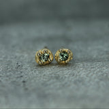 Gold earrings with green sapphires on a gray textured surface