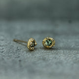 Gold stud earrings with green sapphires on a gray surface