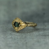 Gold ring with a teal sapphire on a gray surface