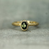 Gold ring with a green sapphire on a textured gray background