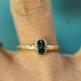 Gold ring with a green sapphire on a finger against a teal background