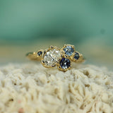 Gold ring with a central diamond and blue gemstones on a textured surface with a blurred green background
