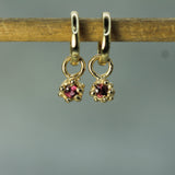 Gold earrings with rubies on a wooden stick against a gray background