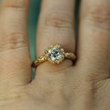 A close-up of a yellow gold ring with a brilliant-cut lab-grown diamond, worn on a person's finger.