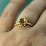 A gold ring with an oval faceted yellow sapphire worn on a finger, shown in a close-up lifestyle shot.