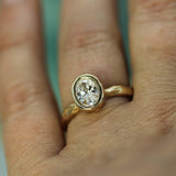 A close-up of a gold ring with a 1ct oval lab-grown diamond worn on a finger.