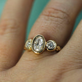 A close-up of a gold ring with a large oval lab-grown diamond center stone and two smaller round lab-grown diamonds on either side, worn on a finger.