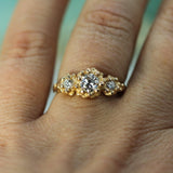 A close-up of a gold three-stone lab-grown diamond ring worn on a finger.